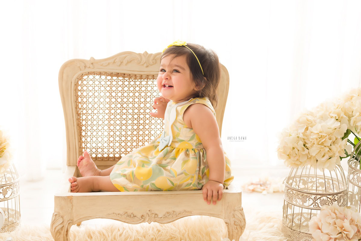 In a picturesque scene painted by Anega Bawa Photography, your 13-month to 1-year-old princess sits serenely on a charming wooden chair. Adorned with delicate ivory flowers and nestled against a backdrop of pristine white castles, she exudes an aura of timeless elegance. Capture these enchanting moments in Delhi and Gurgaon with Anega Bawa Photography.