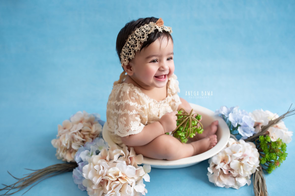 In a delightful photoshoot by Anega Bawa Photography in Delhi and Gurgaon, your 13-month to 1-year-old princess sits elegantly in a white tub adorned with beautiful flowers. Against a serene blue backdrop, her innocence and joy shine through, creating enchanting memories to cherish forever.