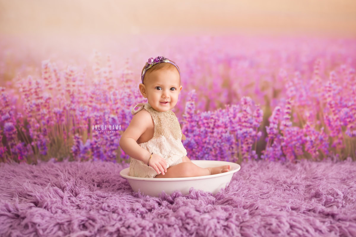 Captured by Anega Bawa Photography in Delhi and Gurgaon, your 13-month to 1-year-old princess sits serenely in a white tub, surrounded by the soothing hues of a lavender backdrop and rug. This enchanting setting perfectly encapsulates her innocence and beauty, creating timeless memories to treasure.