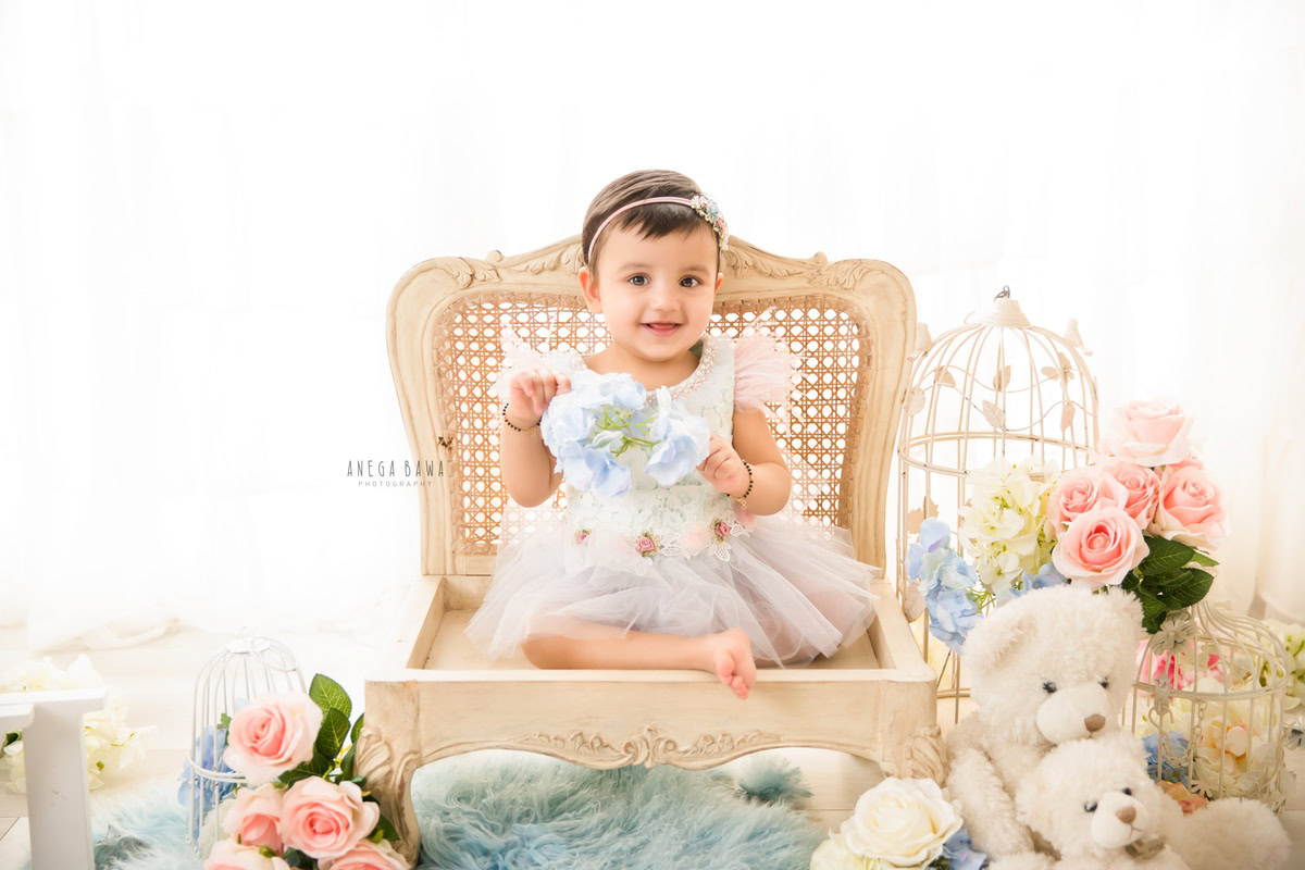 Captured in the serene ambiance of Anega Bawa Photography's studio in Delhi and Gurgaon, your 13-month to 1-year-old princess sits elegantly on a wooden chair against a clean white backdrop. Adorned with white castles and surrounded by a soft blue rug, she exudes charm and innocence, creating timeless memories to treasure for a lifetime.