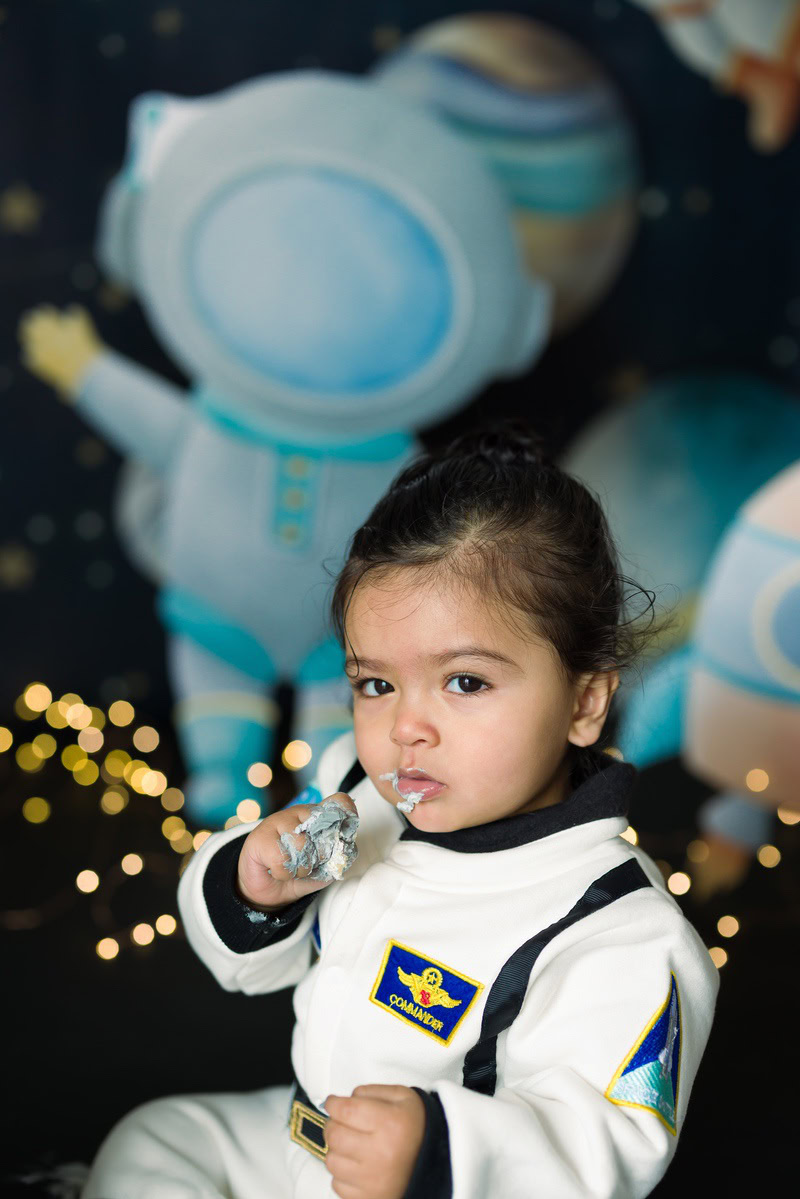 In this enchanting toddler photoshoot by Anega Bawa in Delhi, Gurgaon, and Noida, a delightful girl, aged 14 months to 1 year old, sits amidst twinkling fairy lights against a captivating space backdrop. The ethereal glow of the lights creates a magical atmosphere, complementing the innocence and wonder in the girl's eyes. Anega Bawa expertly captures the beauty and charm of childhood, preserving precious memories that will be cherished for years to come.