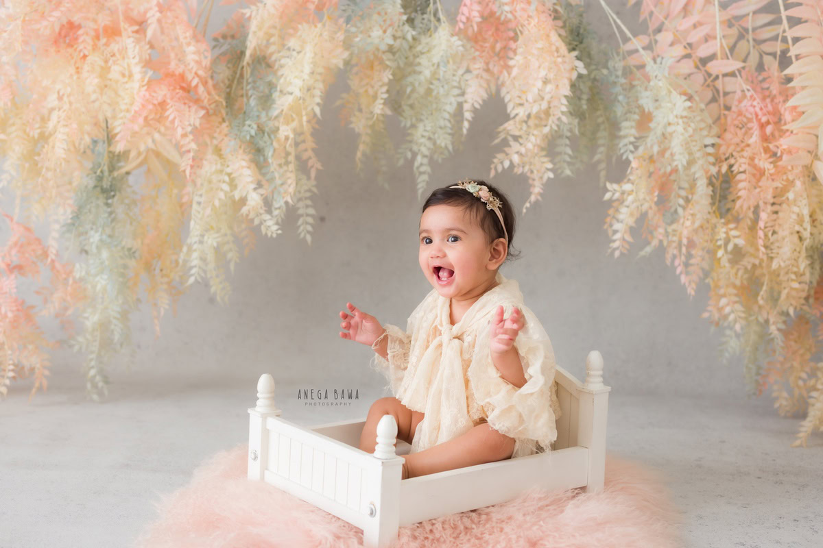 Captured by Anega Bawa in Delhi, Gurgaon, and Noida, this delightful toddler photoshoot features a girl, aged 8 months to 1 year old, sitting snugly in a white cot atop a soft pink rug. The backdrop, adorned with lush greenery, adds a touch of natural beauty to the scene. Through Anega Bawa's lens, the innocence and sweetness of childhood are beautifully preserved, creating cherished memories for years to come.