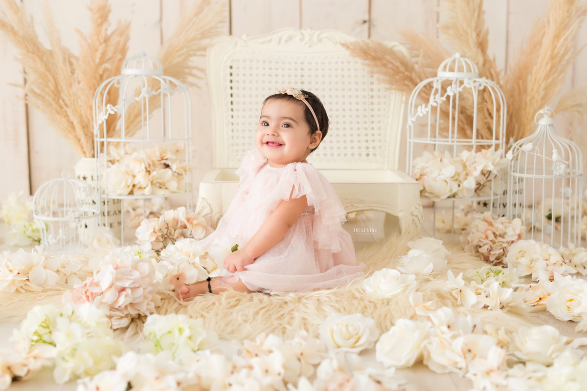 Let Anega Bawa Photography in Delhi and Gurgaon capture the timeless charm of your 15-month to 1-year-old girl. Watch her explore her world seated on a soft beige rug, surrounded by whimsical white castles and lush bushes against a serene beige backdrop. Preserve these precious moments forever with our sitter photography session. Book now!