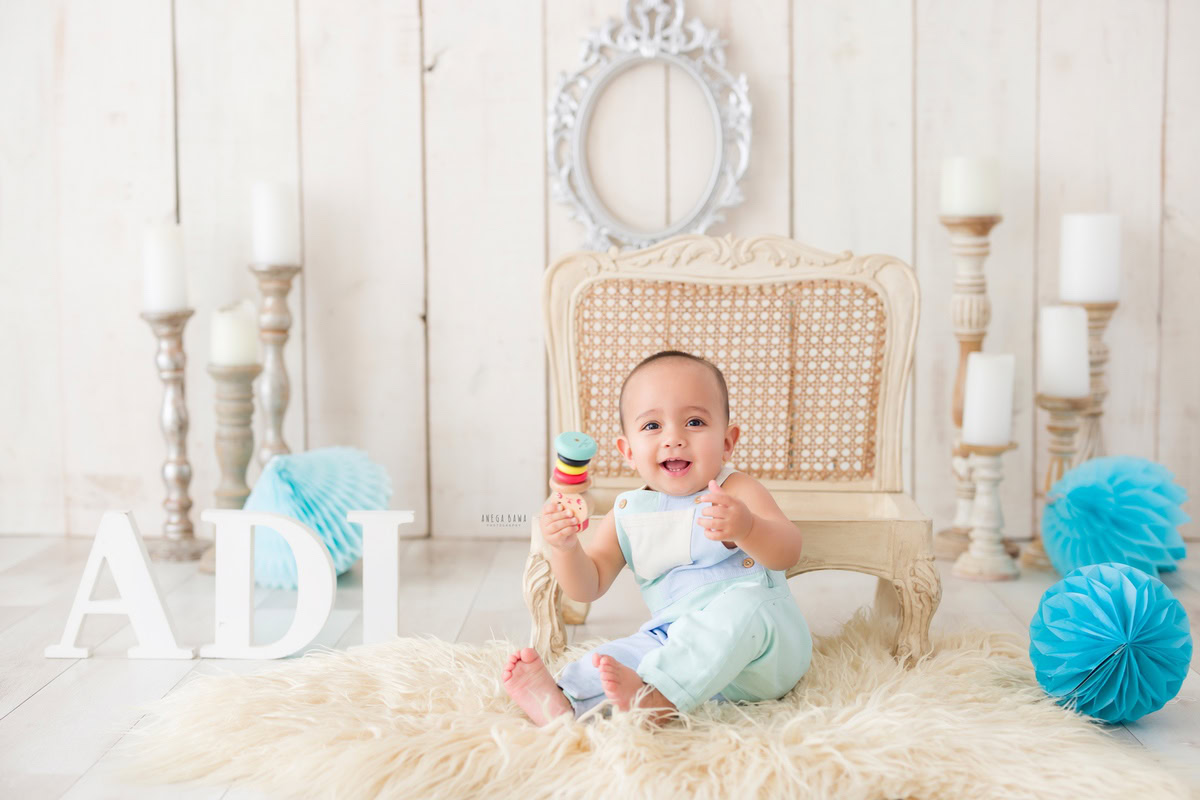 Girl seated on a cozy beige rug on a wooden chair beside a candle stand and pompom, with a silver frame on the wall, marking her journey from 15 months to 1 year old during her first birthday photoshoot in Delhi by Anega Bawa, Gurgaon, Noida.