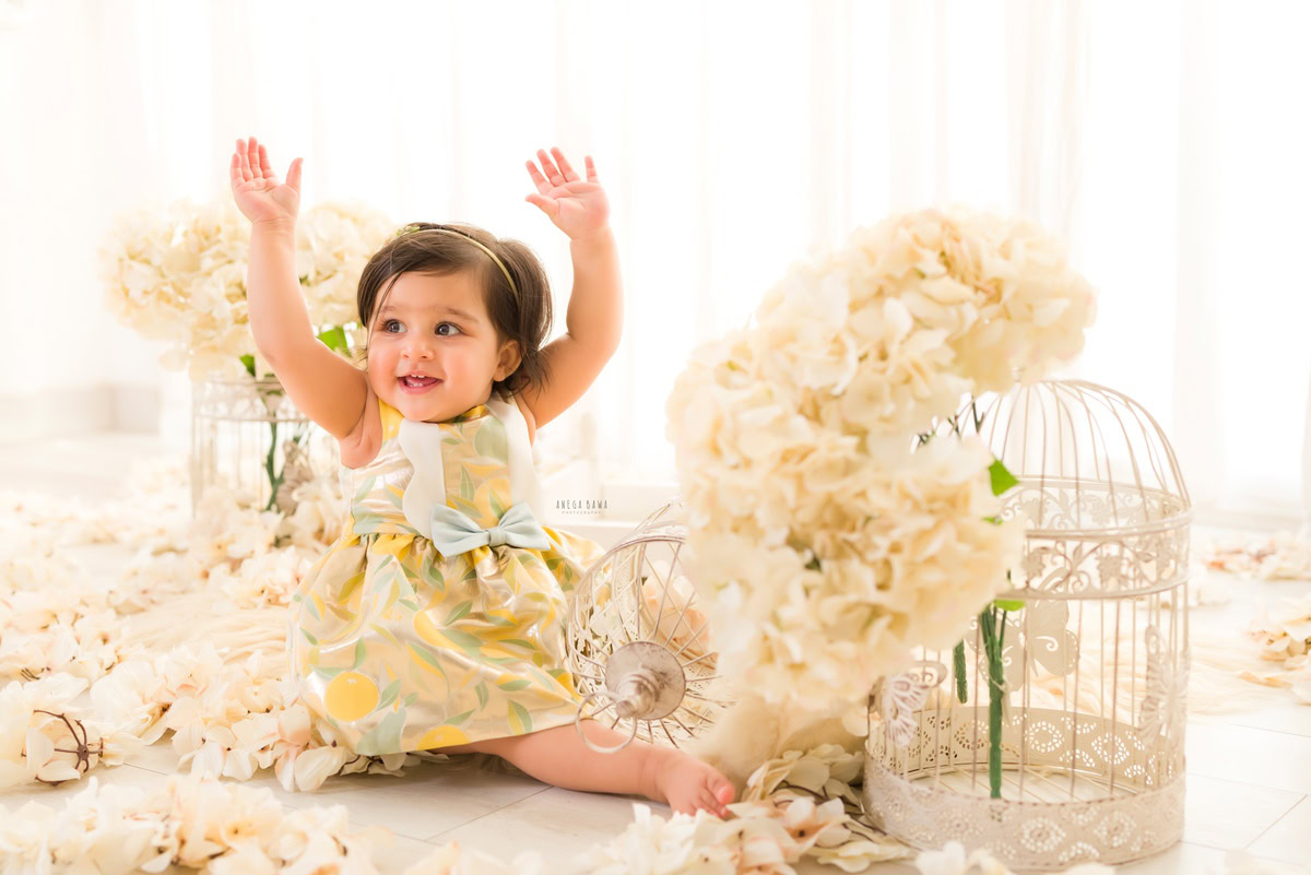 In this enchanting capture by Anega Bawa, a toddler, aged 15 months to 1 year, sits serenely on the floor amidst a backdrop of pristine white castles and ivory flowers. Against a pure white backdrop, the scene exudes a sense of whimsy and innocence, beautifully encapsulating the essence of childhood. Through Anega Bawa's lens, the timeless charm and purity of childhood are elegantly portrayed, creating a heartwarming image that will be cherished for years to come.