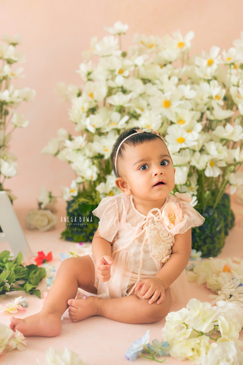 Captured by the talented Anega Bawa, this delightful image features a toddler, aged 7 months to 1 year, seated gracefully on the floor amidst a charming backdrop of delicate white flowers against a soothing peach backdrop. The soft hues and gentle atmosphere evoke a sense of tranquility and innocence, highlighting the beauty of early childhood. Through Anega Bawa's lens, the purity and sweetness of this tender age are beautifully encapsulated, creating a timeless keepsake to be treasured for years to come.