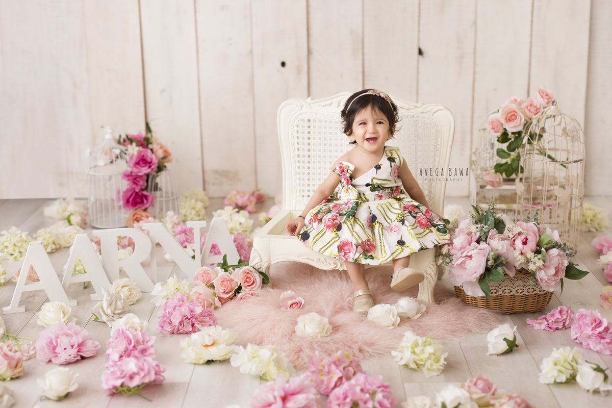 Captured by Anega Bawa in Gurgaon and Delhi, this charming image showcases a 16-month-old girl seated on a white chair against a beige backdrop. Adorned with delicate pink and white flowers, the scene exudes a sense of innocence and beauty. Through Anega Bawa's lens, the timeless essence of childhood is beautifully preserved, creating a cherished memory for years to come.