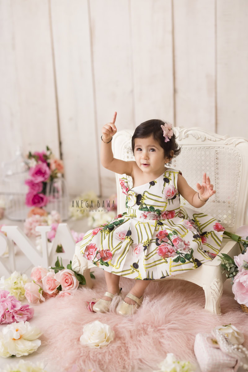 In Gurgaon and Delhi, Anega Bawa beautifully captures the innocence of a 16-month-old girl seated on a white chair, adorned with a pink rug against a soothing beige backdrop. It's a serene moment, expertly crafted to preserve the precious memories of childhood.