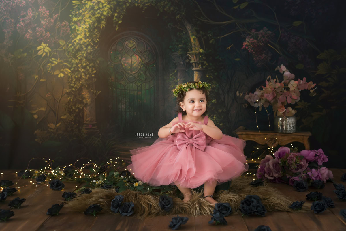 Dressed in a lovely pink outfit adorned with a tiara band, the 17-month-old girl sits gracefully on a soft brown rug. Behind her, a backdrop of leafy brown adds a touch of natural elegance to the scene. Captured by Anega Bawa's lens, this enchanting moment preserves the beauty and innocence of childhood. For timeless portraits that celebrate your little one's milestones, consider sitter photography in Delhi and Gurgaon.