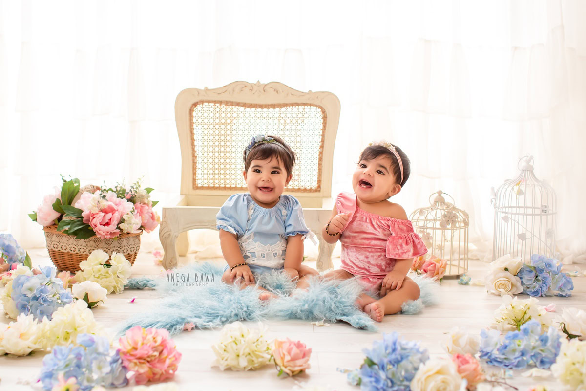 In a delightful photoshoot captured by Anega Bawa Photography in Delhi and Gurgaon, your 17-month to 1-year-old twin girls sit prettily on wooden chairs. Adorned with multicolored flowers and surrounded by whimsical castles, they shine against a pure white backdrop, creating timeless memories filled with innocence and joy.
