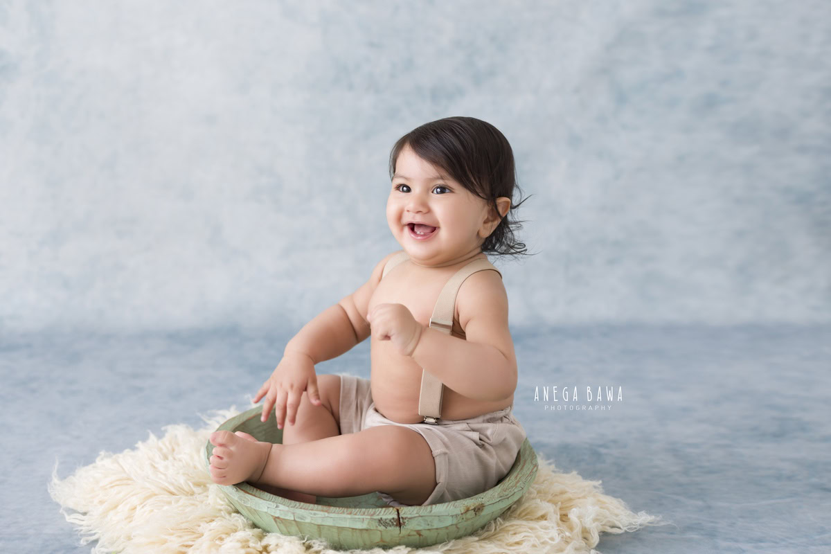 In this delightful toddler photoshoot by Anega Bawa, a 15-month-old boy sits in a tub against a grey-blue backdrop, while a 17-month-old sits nearby. The beige rug adds warmth to the scene, creating a cozy atmosphere for capturing these precious moments in Delhi, Gurgaon, or Noida.