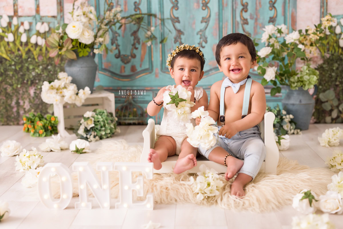 In Gurgaon, Delhi, Anega Bawa beautifully captures the bond between siblings as they sit on a white cot against a backdrop of soothing blue and green hues. Holding a flower between them, they radiate joy and affection, surrounded by delicate white flowers that enhance the purity of the moment.