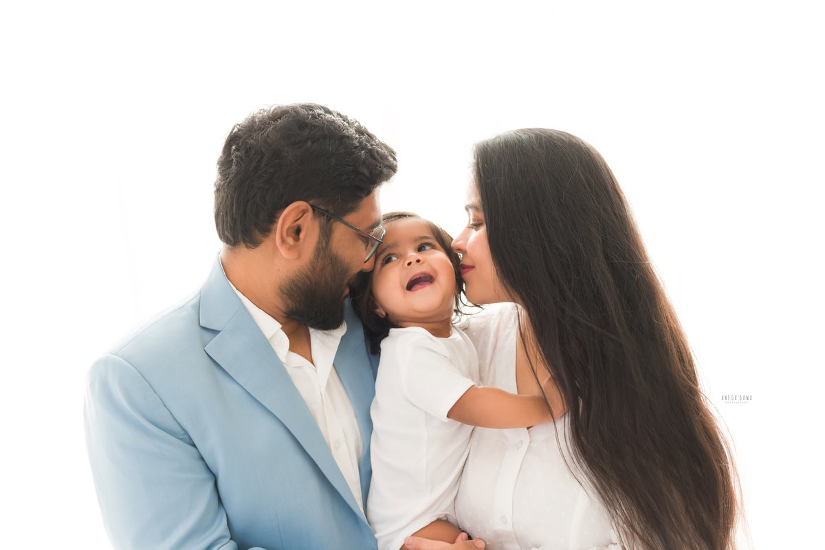 Adorable 1-year-old boy cuddling with mom and dad against a white backdrop, captured by Anega Bawa Family Photographer Gurgaon (Delhi NCR).