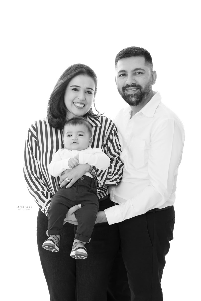 1-year-old boy looking cute in mom's arms, with dad posing beside them against a white backdrop. This beautiful family moment was captured by Anega Bawa Photography in Gurgaon (Delhi NCR).