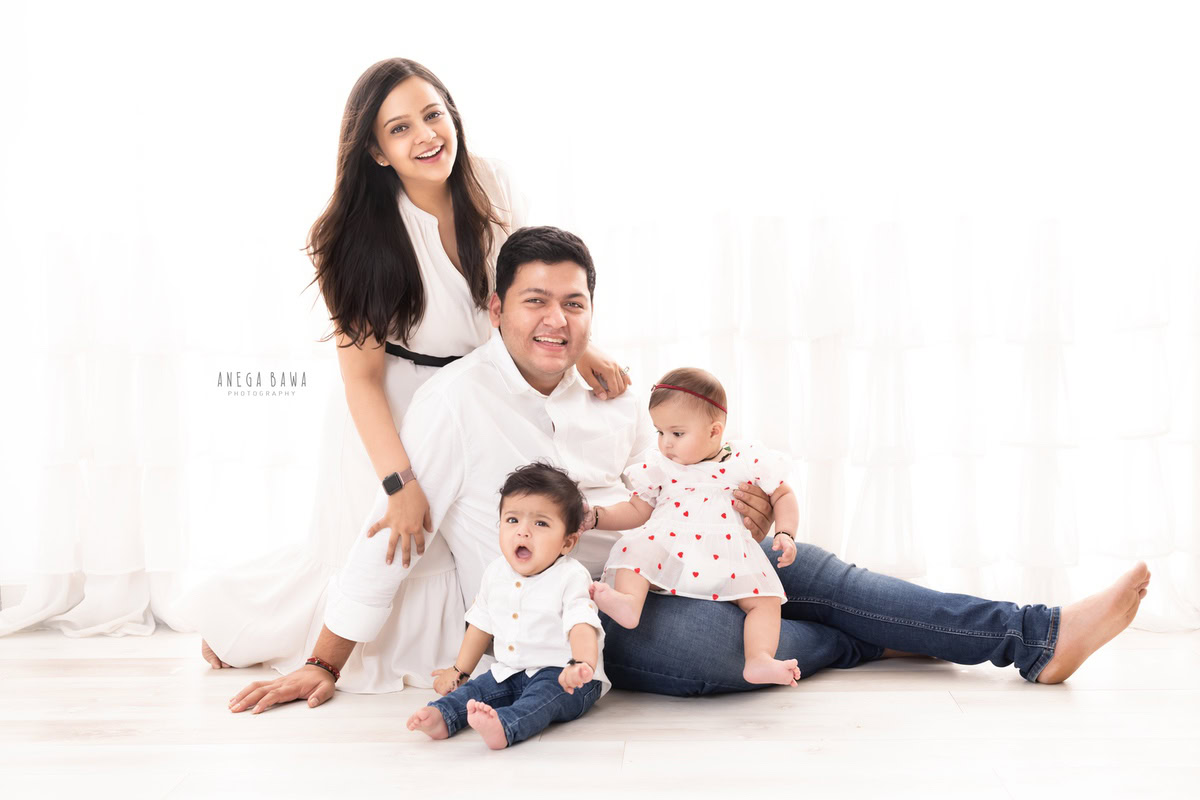 1-year-old boy and girl, posing with their mom and dad, all wearing white outfits against a pristine white backdrop, during a family photo shoot by Anega Bawa Photography in Gurgaon (Delhi NCR)