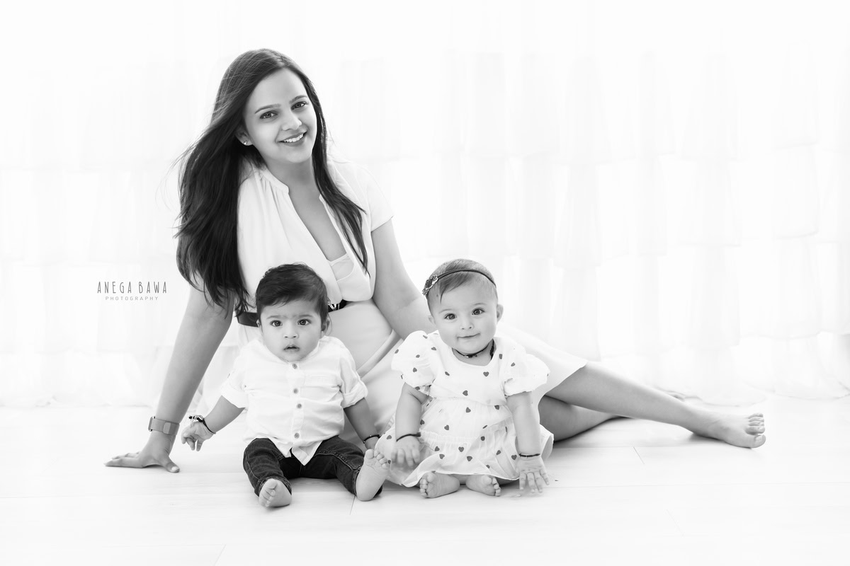 1-year-old boy and girl posing with mom, seated on the floor against a white backdrop. This adorable family moment was captured by Anega Bawa Photography in Gurgaon (Delhi NCR).