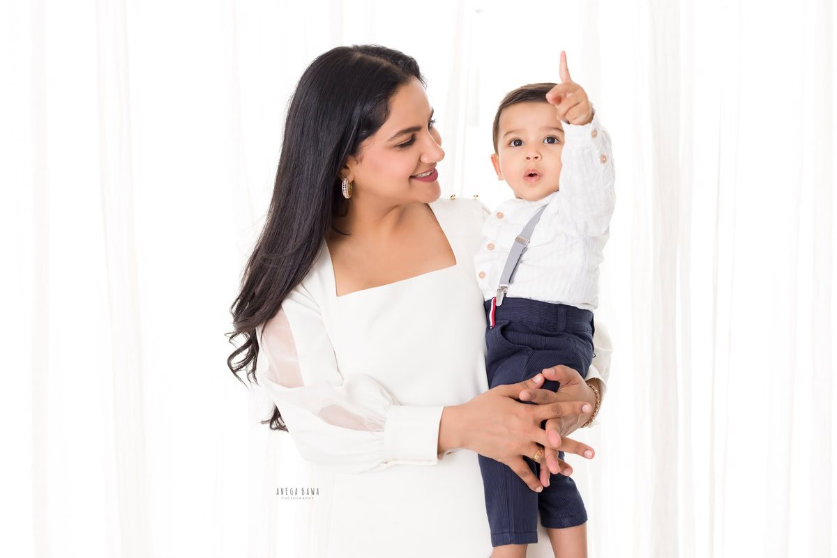 1-year-old boy in mom's arms against a white backdrop, beautifully captured by Anega Bawa Photography during a family photoshoot in Gurgaon (Delhi NCR).