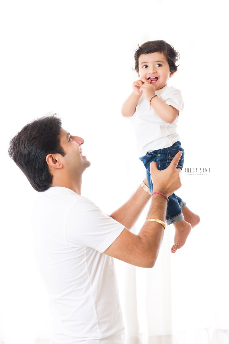 1-year-old boy lifted in dad's arms against a white backdrop. Captured by Anega Bawa Photography, Gurgaon (Delhi NCR).