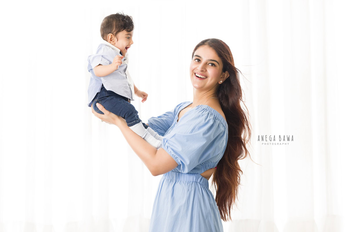 1-year-old boy joyfully lifted in mom's arms against a white backdrop. Captured by Anega Bawa Photography, Gurgaon (Delhi NCR).