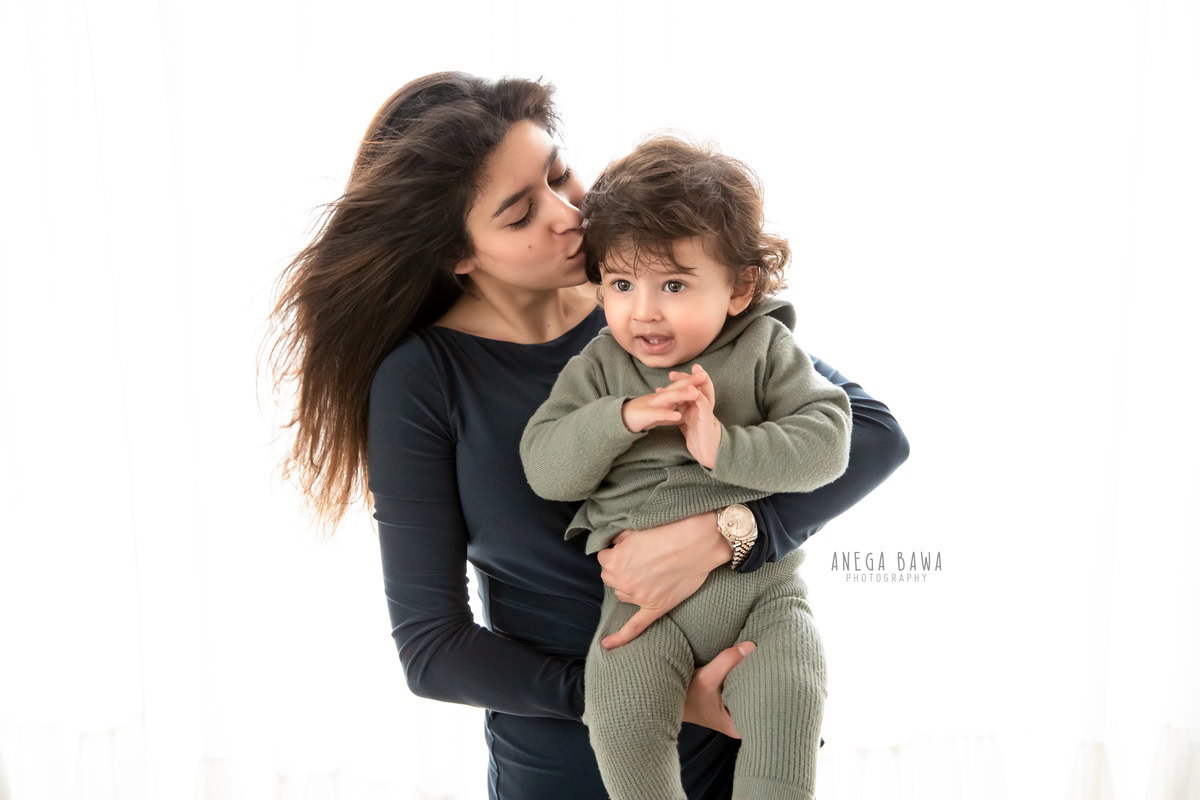 1-year-old boy in a cute kissing pose with mom against a white backdrop. Capture these tender moments with Anega Bawa Photography, the specialist in family photo shoots in Gurgaon (Delhi NCR).
