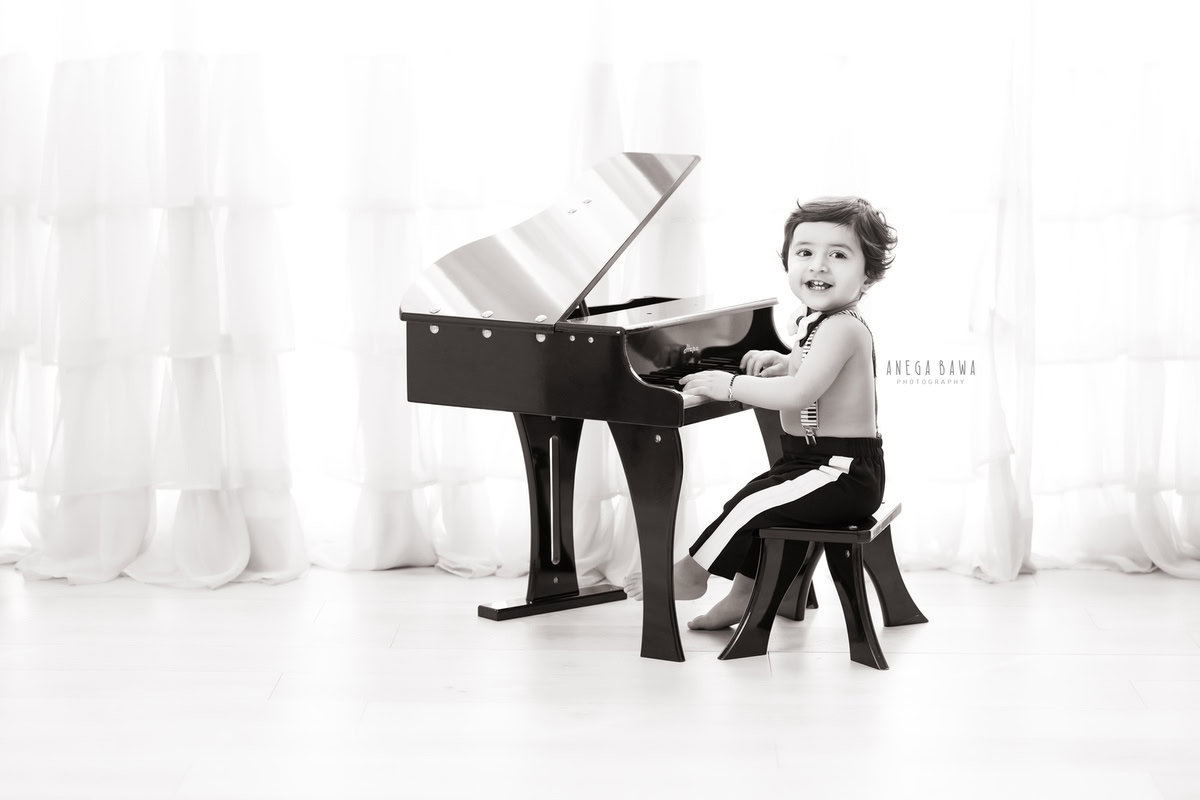 1-year-old boy playing the piano against a white backdrop, beautifully captured by Anega Bawa Photography during a family photoshoot in Gurgaon (Delhi NCR).