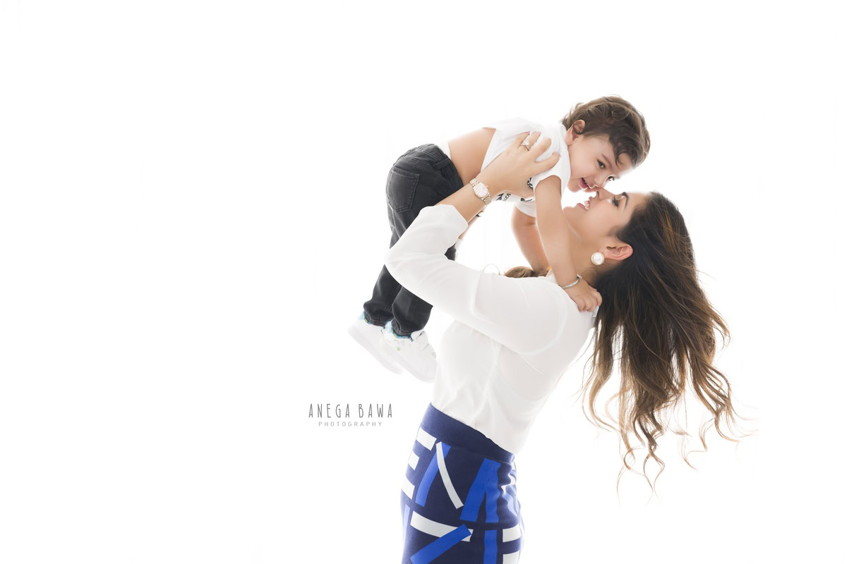 1-year-old boy playfully interacting with mom against a white backdrop. Captured by Anega Bawa Photography, Gurgaon (Delhi NCR).