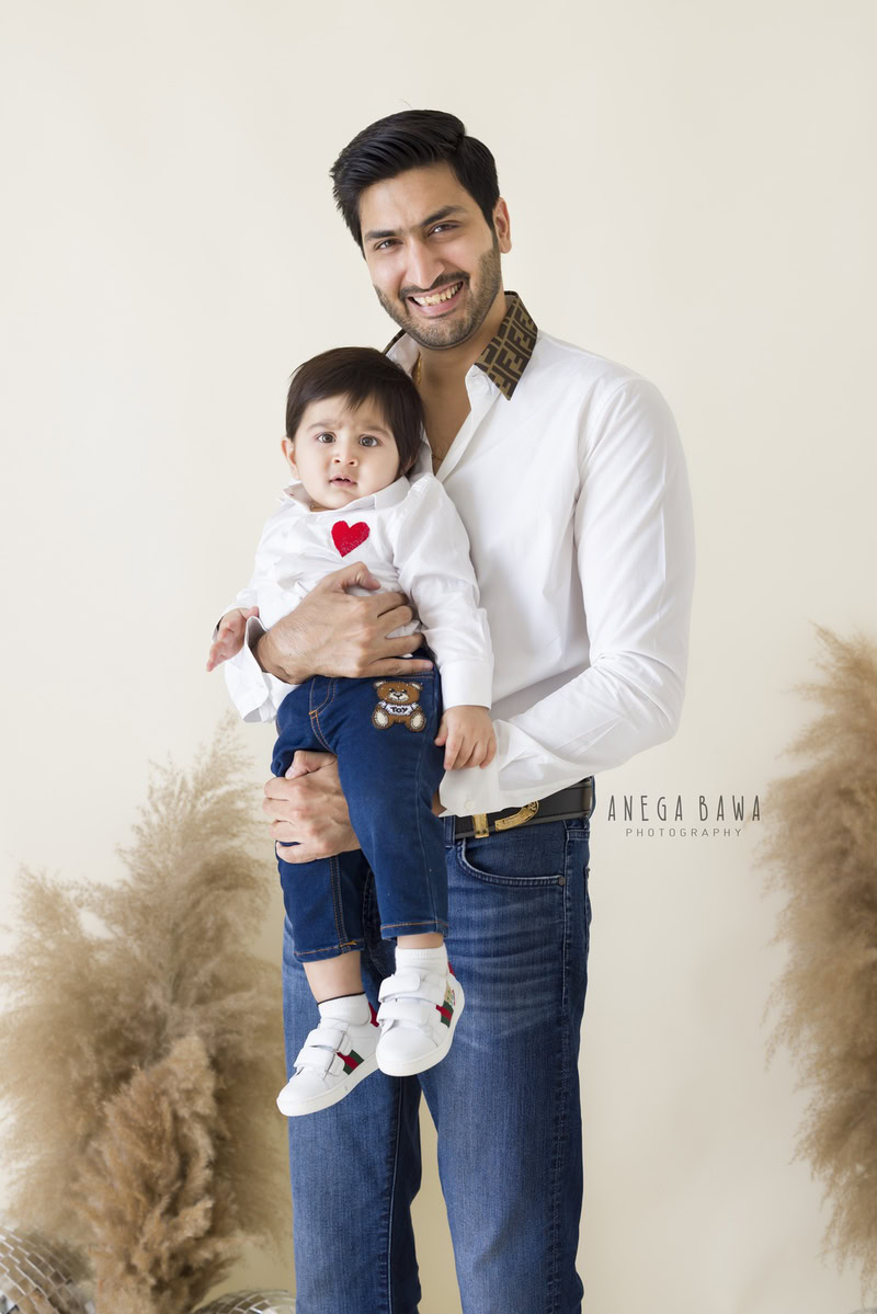 1-year-old boy posing with dad against a backdrop of bushes on a beige background. Captured by Anega Bawa Photography, Gurgaon (Delhi NCR).