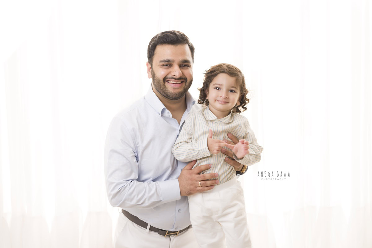 Charming 1-year-old boy posing with dad in a smiling pose against a white backdrop, captured by Anega Bawa Family Photographer Gurgaon (Delhi NCR).