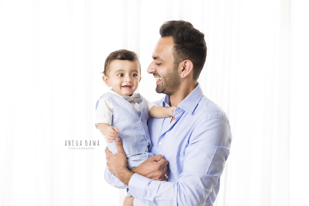 1-year-old boy posing with dad in a smiling pose against a white backdrop. Captured by Anega Bawa Photography, Gurgaon (Delhi NCR).