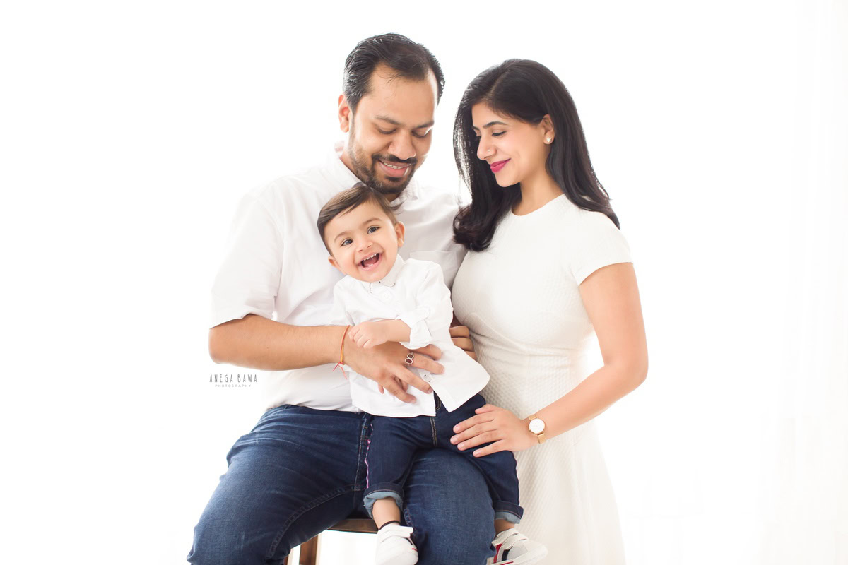 1-year-old boy poses with mom and dad, all wearing white, against a white backdrop, family photoshoot in Gurgaon (Delhi NCR)