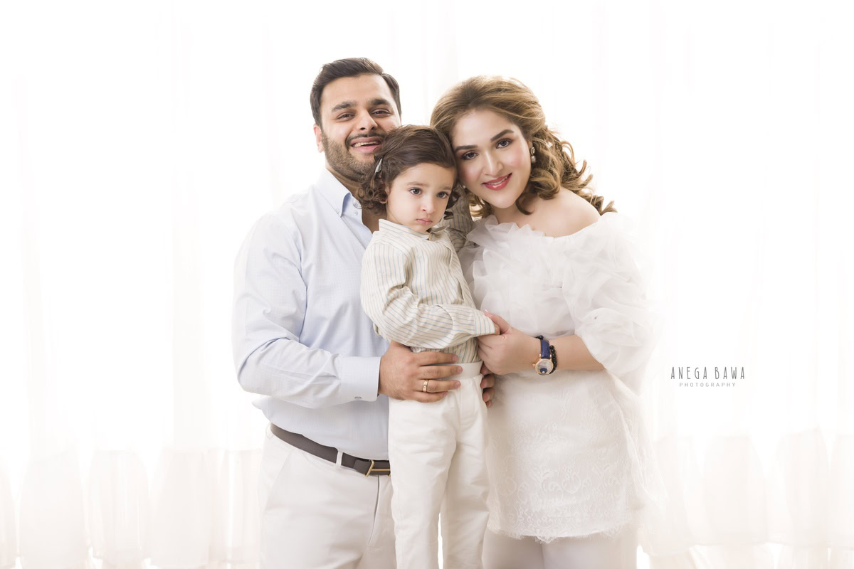 Adorable 1-year-old boy posing with mom and dad against a white backdrop, captured by Anega Bawa Family Photographer Gurgaon (Delhi NCR).