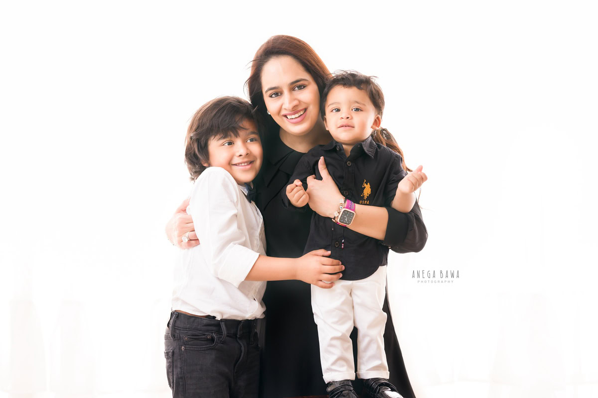 1-year-old boy posing with mom and elder brother in a sweet hugging pose against a white backdrop. Family photo shoot is done by Anega Bawa Photography in Gurgaon (Delhi NCR) to capture these cherished moments.