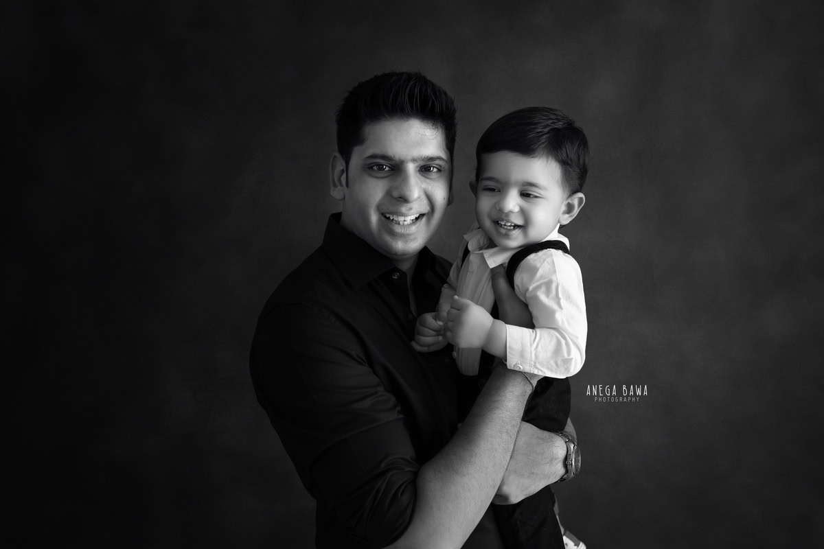 1-year-old boy posing cutely with dad against a black backdrop, beautifully captured by Anega Bawa Photography for a family photoshoot in Gurgaon (Delhi NCR).