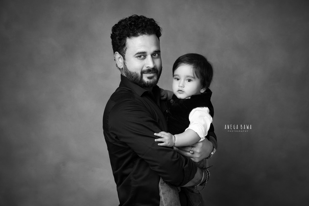 Cute 1-year-old boy posing with dad against a black and white backdrop, captured by Anega Bawa Family Photographer Gurgaon (Delhi NCR).