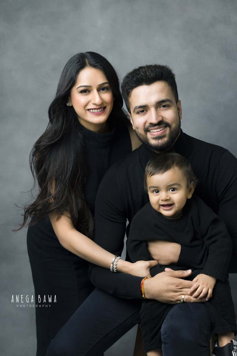 1-year-old boy posing cutely with mom and dad, all wearing black, against a grey backdrop, family photoshoot in Gurgaon (Delhi NCR)