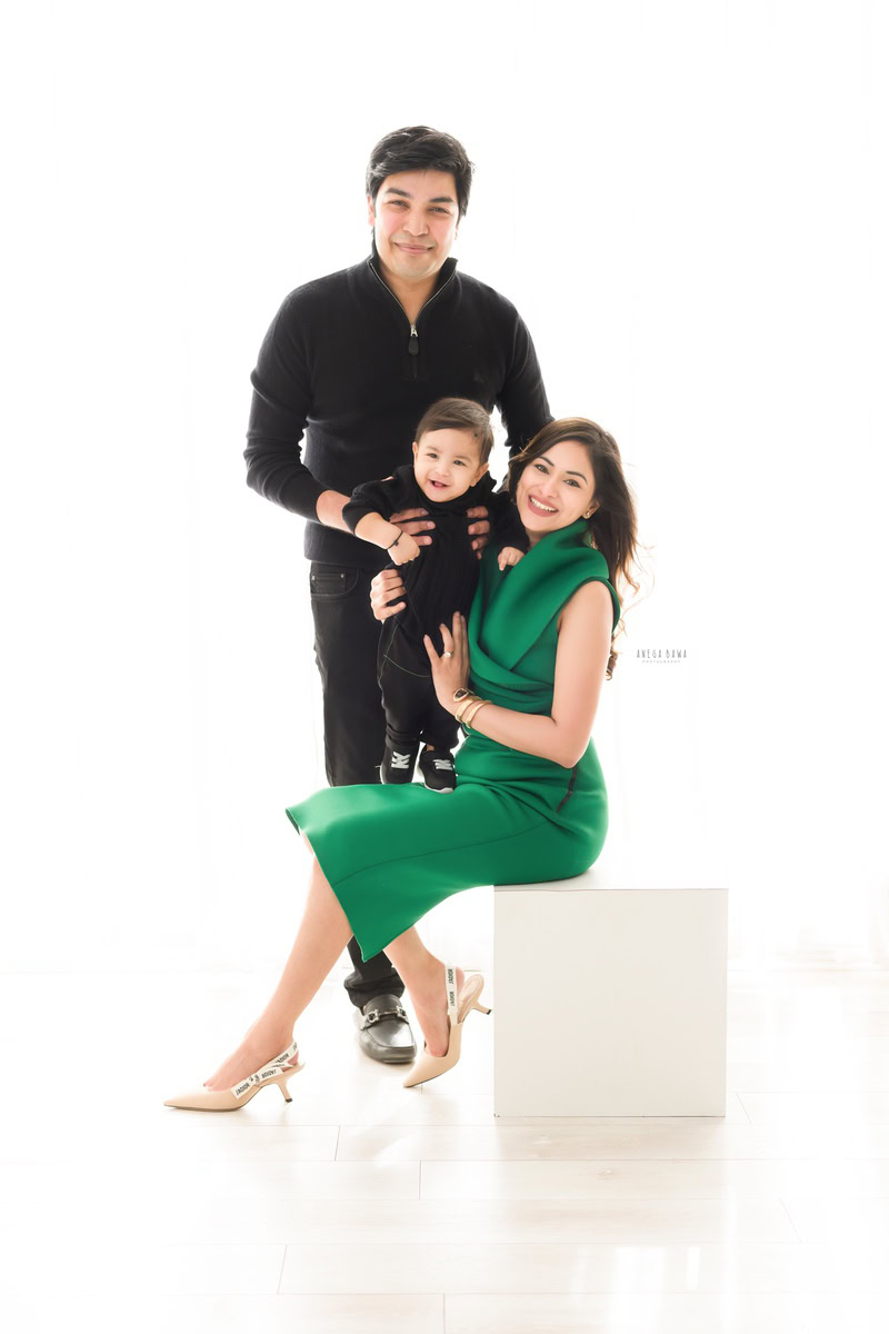 1-year-old boy posing cutely with mom and dad against a serene white backdrop, beautifully captured by Anega Bawa Photography for a family photoshoot in Gurgaon (Delhi NCR).