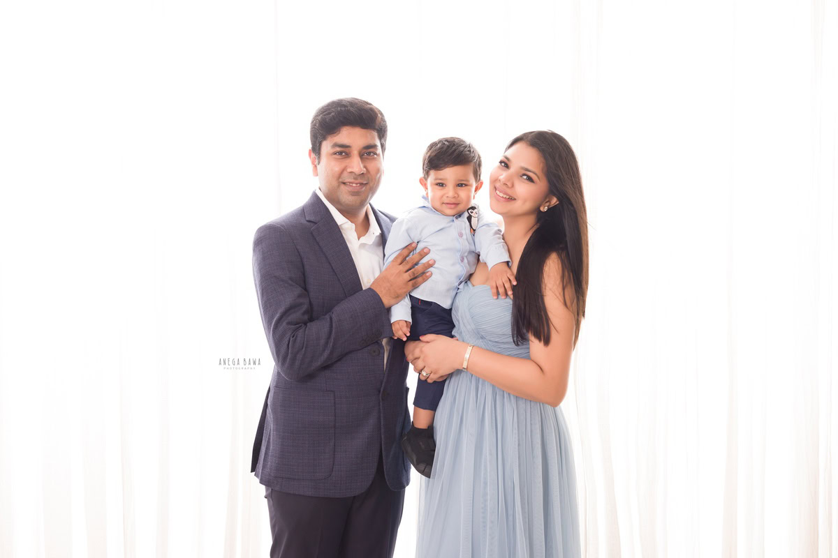 Adorable 1-year-old boy posing cutely with mom and dad against a white backdrop, captured by Anega Bawa Family Photographer Gurgaon (Delhi NCR).