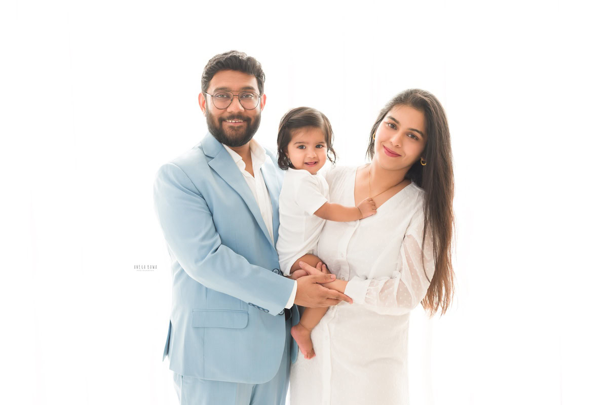 1-year-old boy posing cutely with mom and dad against a serene white backdrop, captured by Anega Bawa Photography for a family photoshoot in Gurgaon (Delhi NCR).