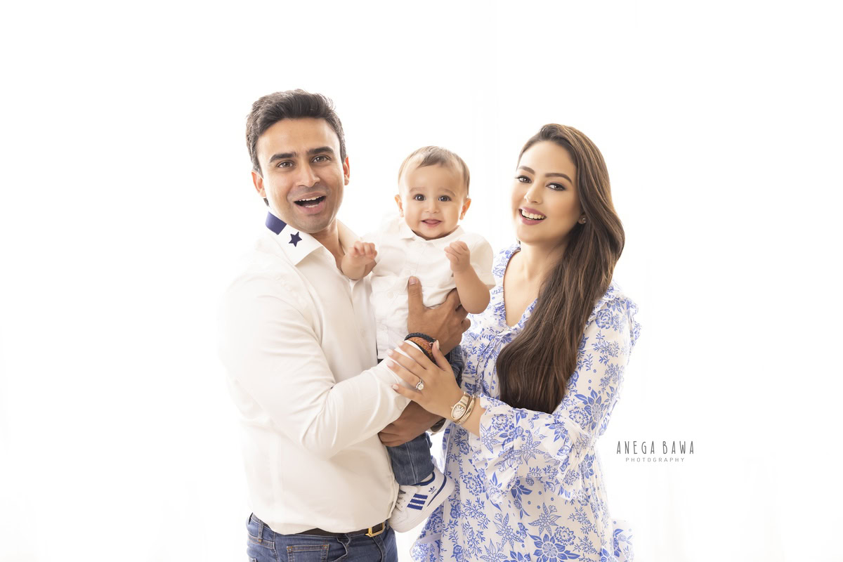 1-year-old boy posing cute with mom and dad against a white backdrop. This delightful family photo shoot is done by Anega Bawa Photography in Gurgaon (Delhi NCR), preserving precious memories.
