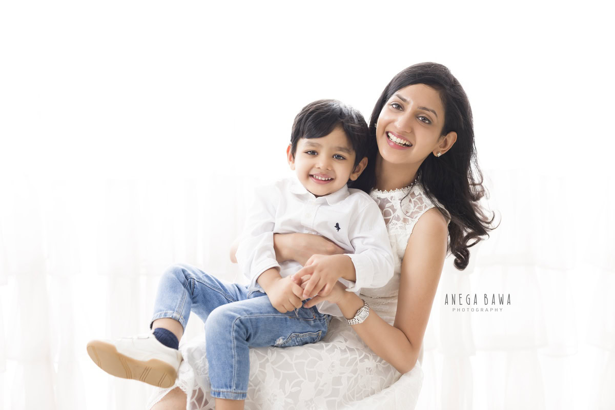 1-year-old boy posing on mom's lap against a white backdrop. Captured by Anega Bawa Photography, Gurgaon (Delhi NCR).