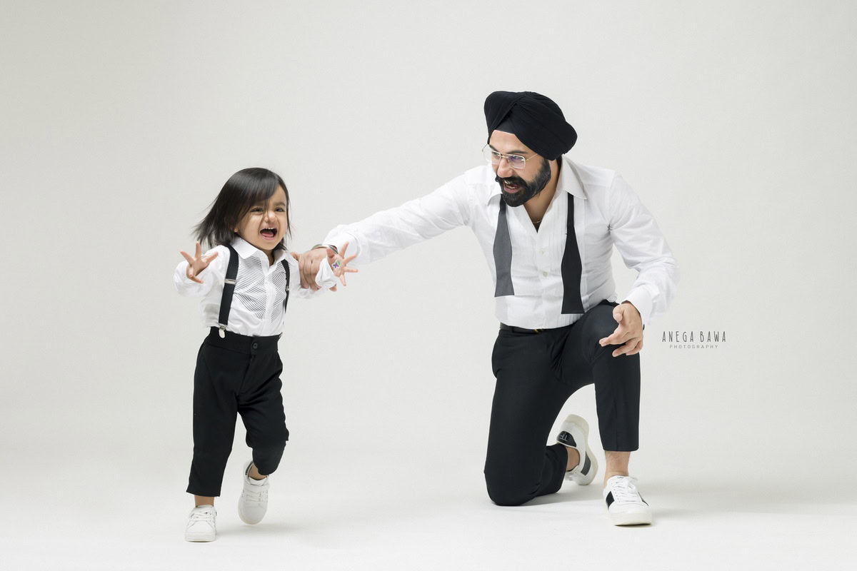 1-year-old boy posing, twinning with dad in a white shirt and black trousers against a white backdrop. Captured by Anega Bawa Photography, Gurgaon (Delhi NCR).
