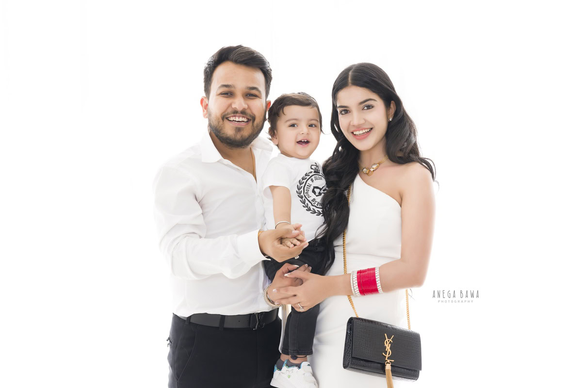 Adorable 1-year-old boy posing with his aunt and uncle against a white backdrop, captured by Anega Bawa Family Photographer Gurgaon (Delhi NCR).