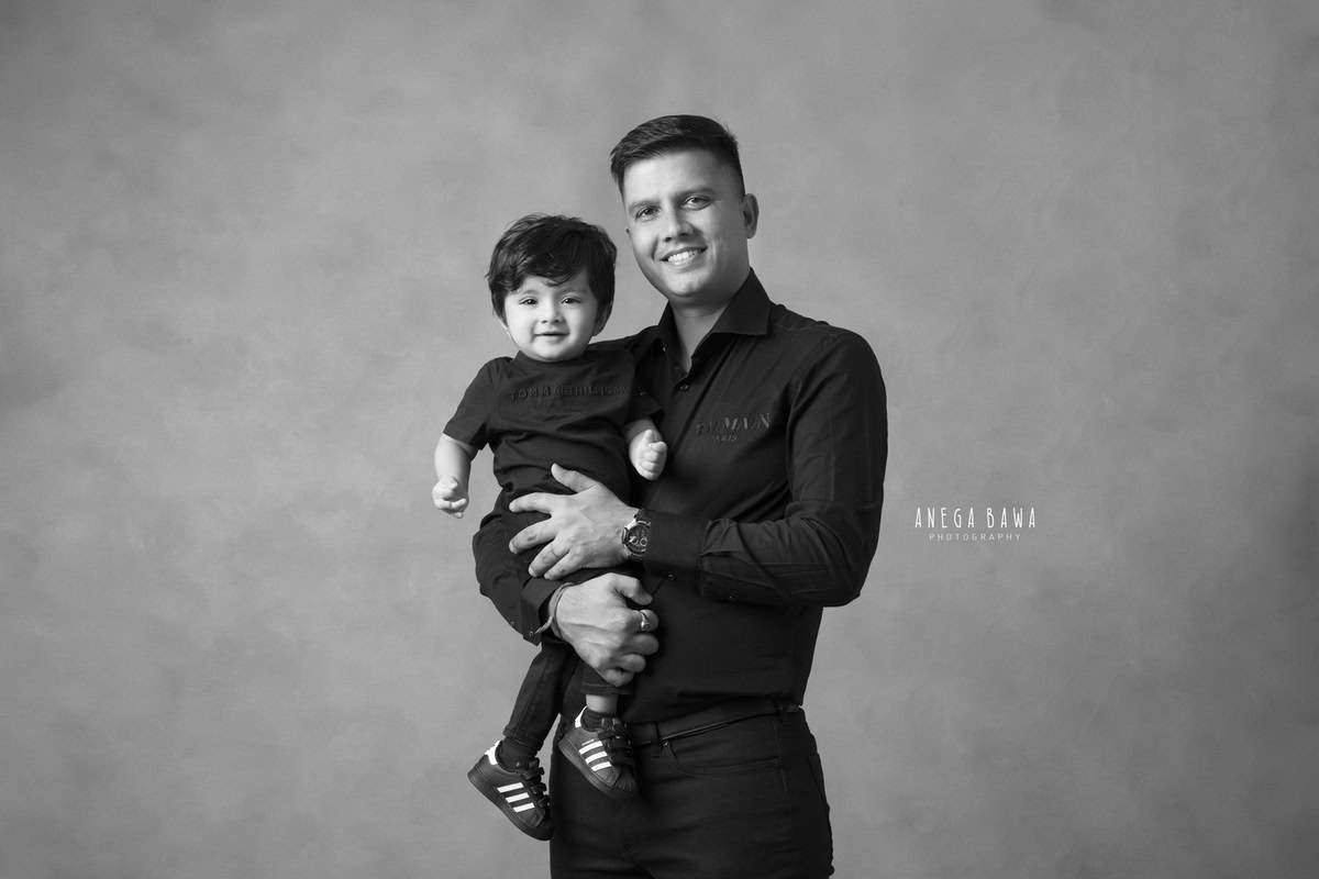 1-year-old boy posing with dad against a grey backdrop. Capture this heartwarming moment with Anega Bawa Photography, your go-to expert for family photo shoots in Gurgaon (Delhi NCR).