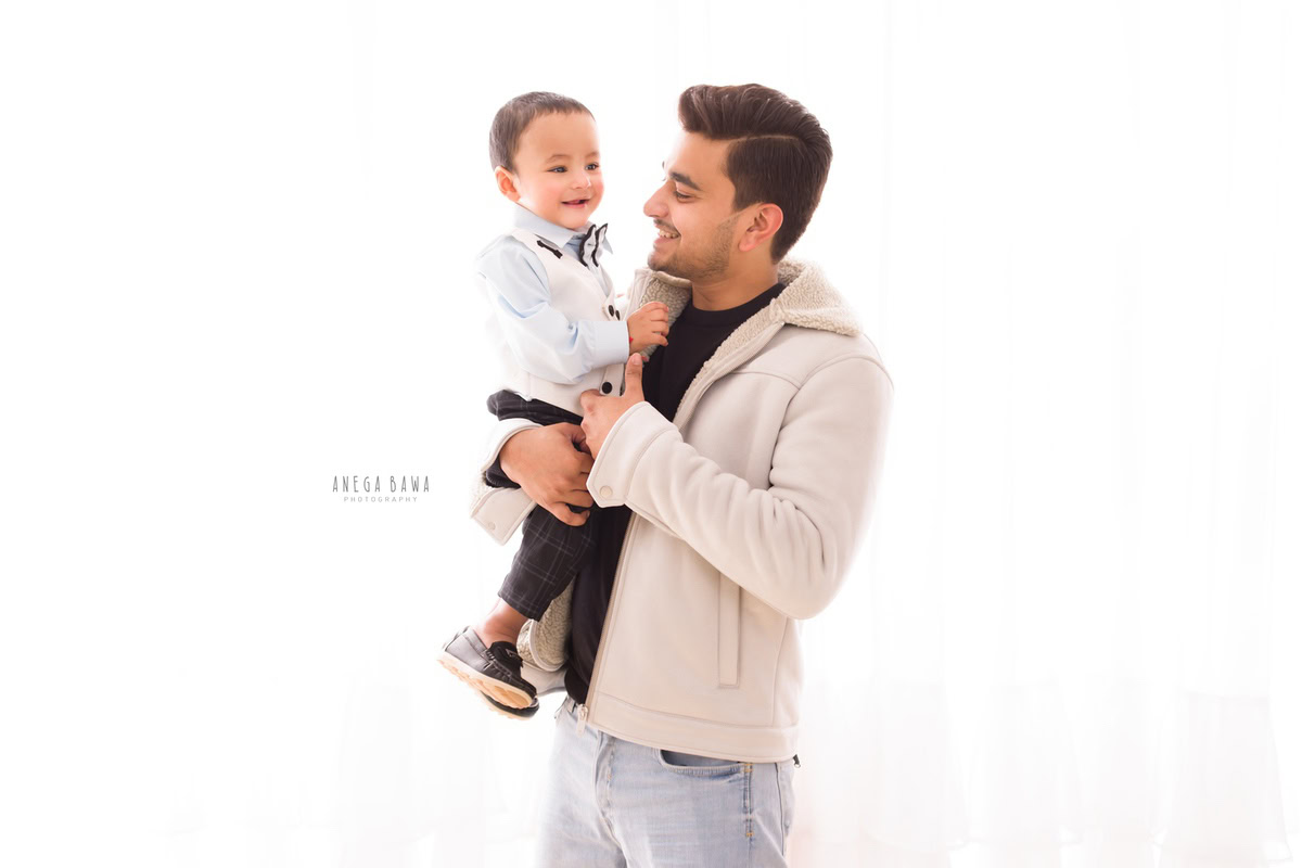 1-year-old boy confidently posing with his dad against a pristine white backdrop. Professionally captured by Anega Bawa Photography, Gurgaon (Delhi NCR).