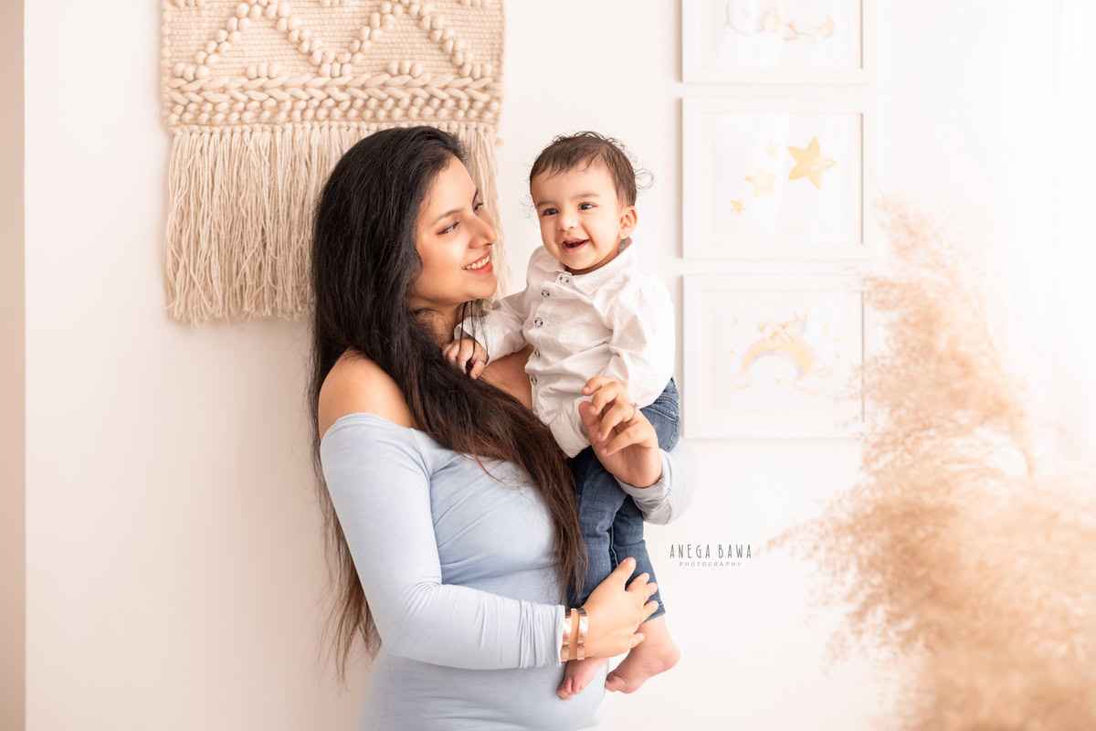 1-year-old boy posing with mom against a backdrop of bushes and beige scenery, captured by Anega Bawa Family Photographer Gurgaon (Delhi NCR).