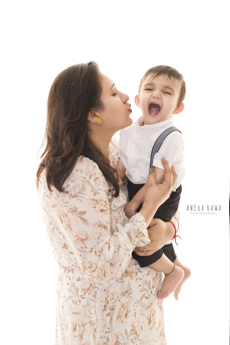 Cute 1-year-old boy posing with mom in a smiling pose against a white backdrop, captured by Anega Bawa Family Photographer Gurgaon (Delhi NCR).