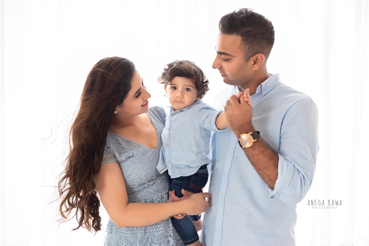 1-year-boy posing with mom and dad, all wearing blue, against a serene white backdrop, beautifully captured by Anega Bawa Photography for a family photoshoot in Gurgaon (Delhi NCR).