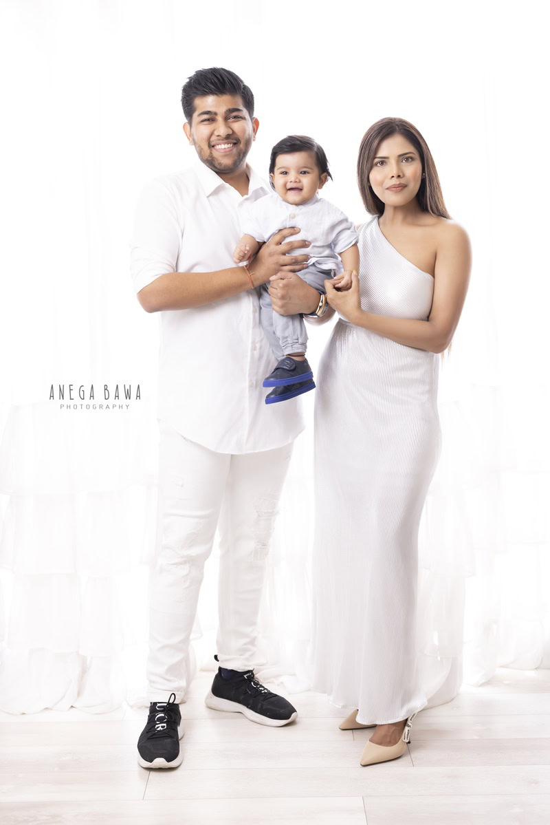 1-year-old boy posing with mom and dad, all dressed in white, against a white backdrop. Captured by Anega Bawa Photography, Gurgaon (Delhi NCR).