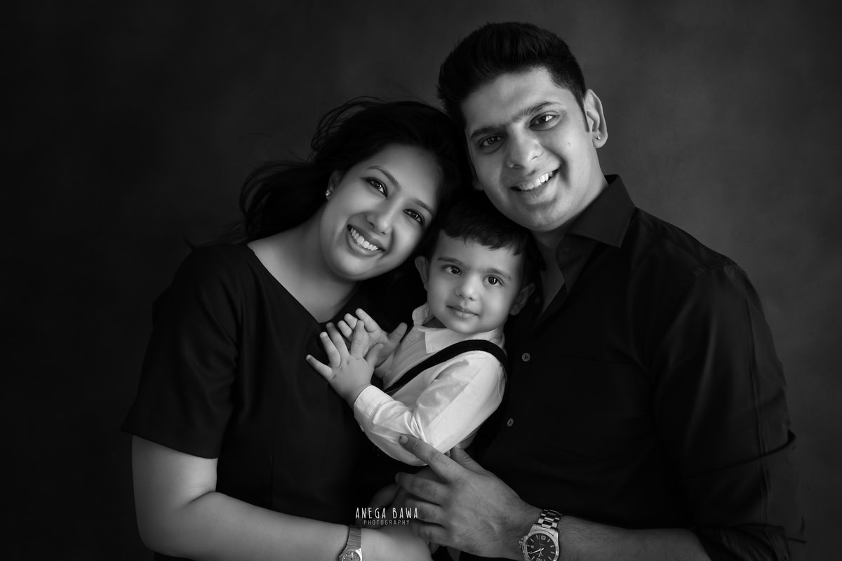 1-year-old boy posing with mom and dad against a black backdrop, the boy wearing a white shirt, captured by Anega Bawa Family Photographer Gurgaon (Delhi NCR).