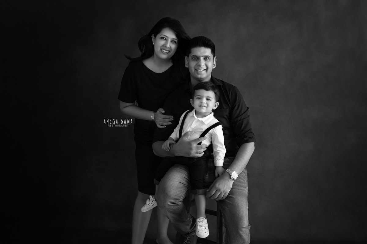 1-year-old boy posing with mom and dad against a sleek black backdrop. Captured by Anega Bawa Photography, Gurgaon (Delhi NCR).